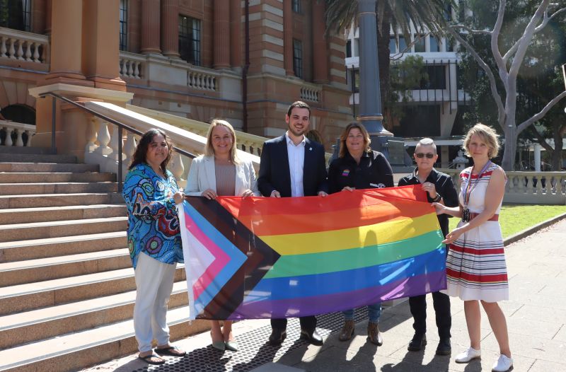 Indigenous leader Aunty Theresa Dargin, Lord Mayor Nuatali Nelmes, Deputy Lord Mayor Declan Clausen, Newcastle Pride President Lee-Anne McDougall, Newcastle Pride Vice President Hellen Richards and City of Newcastle Diversity and Inclusion Partner Stefanie Abrahams with the Progress Pride Flag before it was raised at City Hall in February 2022.