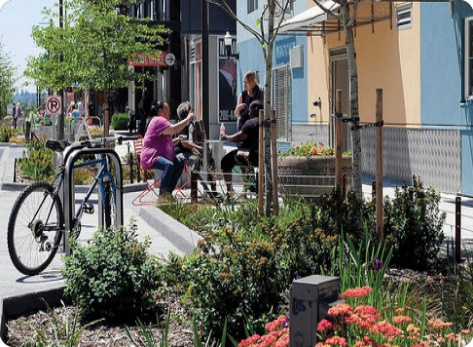 People sitting outside at a café, with a small planting area. There is a bike parked next to the planting area.