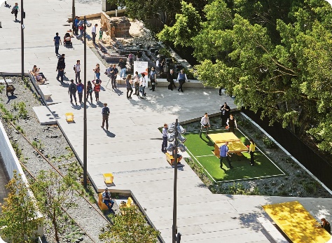 A birds-eye view of people walking on a pedestrian path, with trees and people playing at a table tennis table.