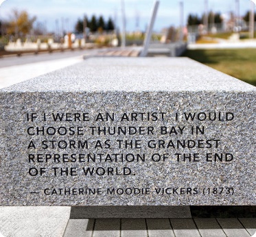 A bench with a quote on it. It says ”If I were an artist, I would choose thunder bay in a stream as the grandest representation of the end of the world.”