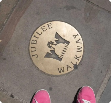 Feet standing at a sign on the footpath that says “Jubilee Walkway”.