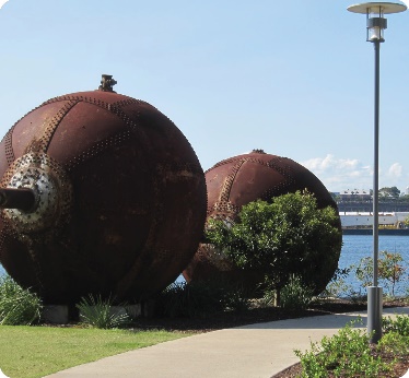 Big, old, rusted metal spheres next to a footpath.
