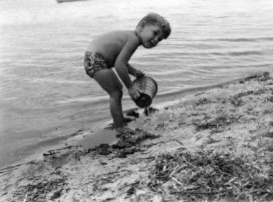 Little boy with a sand bucket by the lake