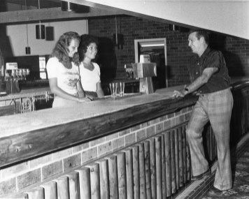 Man leaning at bar chatting with 2 female bartenders